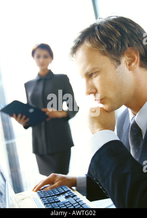 Businesswoman standing in fond, floue, à la recherche d'affaires à assis à l'ordinateur, Banque D'Images