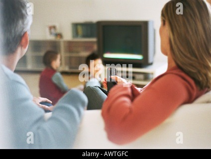 Les parents sitting on sofa holding remote control pendant que les enfants s'asseoir près de la télévision Banque D'Images