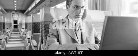 Businessman sitting in train using laptop, b&w, vue panoramique Banque D'Images