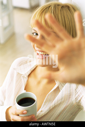 Teen girl with coffee holding main devant le visage, laughing Banque D'Images