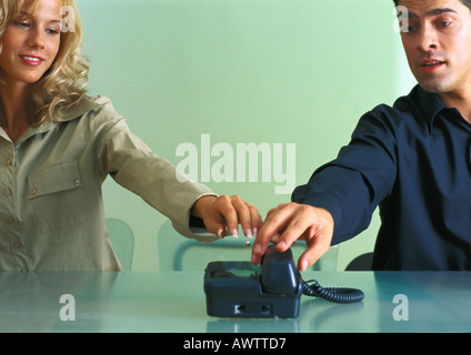 Couple à table, à la fois atteindre pour répondre téléphone au même moment Banque D'Images