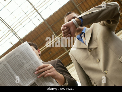 Deux hommes d'affaires, l'un avec du papier journal, d'autres contrôler watch, low angle Banque D'Images