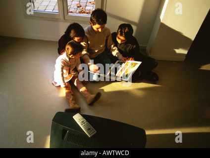 Les jeunes garçons et filles assis sur marbre regardant un livre, high angle view Banque D'Images