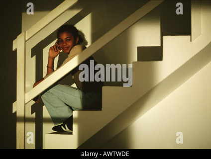 Jeune fille assise sur l'escalier, parlant au téléphone, smiling Banque D'Images