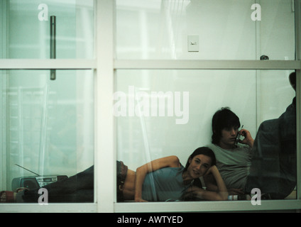 Woman lying on floor next to man on cell phone Banque D'Images