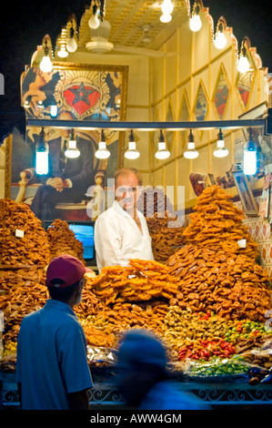 Portrait vertical d'un homme âgé qui sert derrière un écran de sucreries et pâtisseries marocaines traditionnelles dans la rue SOUK SMARINE Banque D'Images