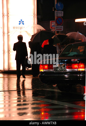 Hommes d'arriver à Tokyo ville pluvieuse humide rue la nuit avec parasols Banque D'Images