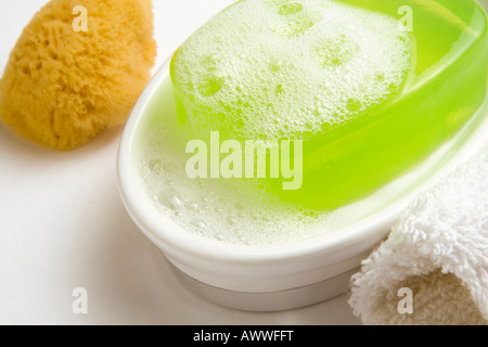 Une barre de couleur citron vert savon glycérine avec la mousse sur un plat de savon blanc avec blanc tissu de lavage et la beauté d'une éponge Banque D'Images