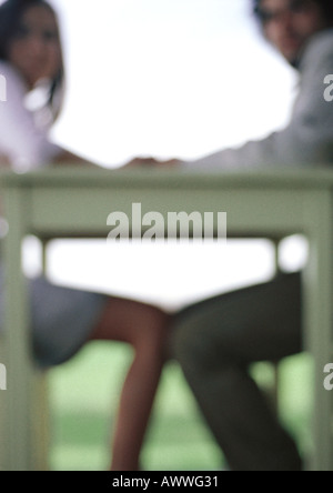 Young couple sitting at table tenant les mains, silhouette floue Banque D'Images