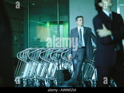 Hommes d'debout devant l'aéroport de chariots à bagages. Banque D'Images