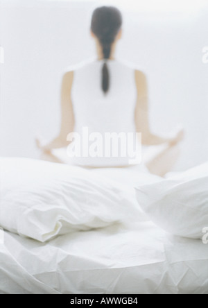 Woman sitting in lotus position sur lit, vue arrière, blurred Banque D'Images