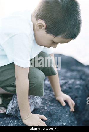 Enfant accroupi sur rock, close-up Banque D'Images