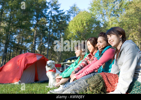 Quatre adolescentes assis sur l'herbe côte à côte, le camping Banque D'Images