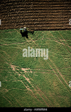 Un agriculteur sur un grand tracteur John Deere laboure un champ d'herbe verte dans le coeur des États-Unis d'Amérique. Banque D'Images