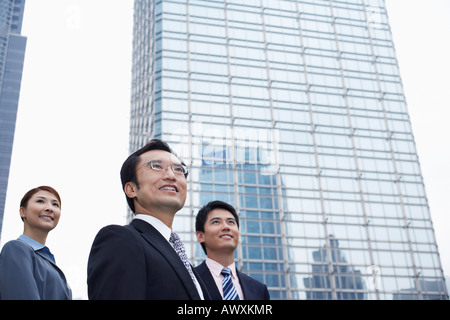 La Chine, Hong Kong, trois personnes debout entre les gratte-ciel, low angle view Banque D'Images