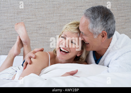 Middle-aged couple lying on bed, laughing Banque D'Images