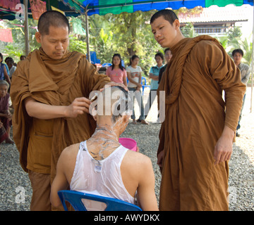 Deux moines bouddhistes thaïlandais utiliser un rasoir pour raser la tête d'une jeune Thai man, une partie de l'ordination d'un moine novice Banque D'Images