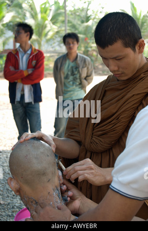 Un moine bouddhiste thaï utilise un rasoir pour se raser la tête d'une jeune thai man partie de l'ordination d'un moine novice Banque D'Images