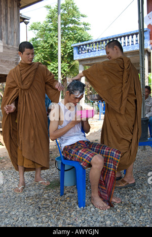 Deux moines bouddhistes thaïlandais utilisez de l'eau savonneuse pour préparer un jeune homme thaïlandais pour le rasage de la tête, une partie de l'ordination d'un moine novice Banque D'Images