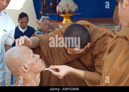 En tant que membres de la famille montre, un moine bouddhiste thaï se rase le menton d'une jeune Thai man, une partie de l'ordination d'un moine novice Banque D'Images