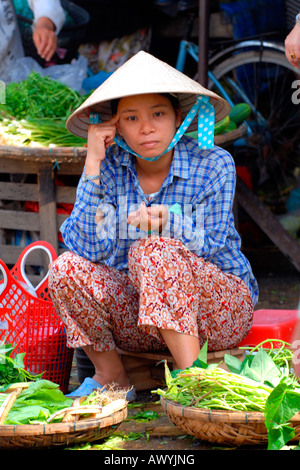 Asie extrême-Orient Asie extrême-Orient ietnam , marché Hoi an , jeune fille pensive dans non bai tho et robe nationale vendant des légumes feuilles de la stalle de chaussée Banque D'Images