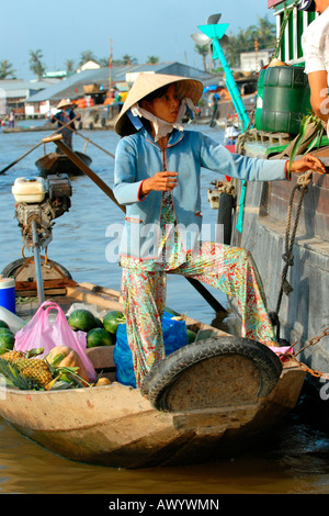 Marché flottant du Delta du Mékong au Vietnam , jeune femme en costume national la vente de bananes et ananas , mandarins de voile Banque D'Images