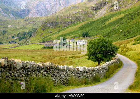 Route qui serpente à travers le pays de Galles Snowdonia Nnant Ffrancon Valley avec un cottage dans la distance blanchis Banque D'Images