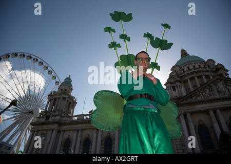 Stiltwalker habillé en vert portant des trèfles à Belfast City Hall et grande roue avant la parade et le carnaval St Patricks day Banque D'Images