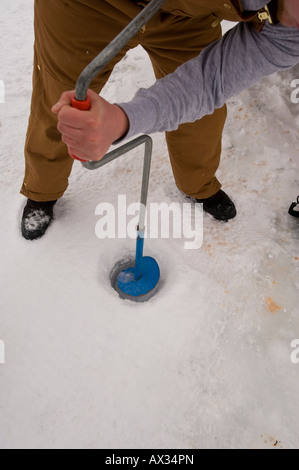 Un homme PERCE UN TROU DANS LA GLACE ÉPAISSE AVEC LA VIS DE GLACE MANUEL Banque D'Images