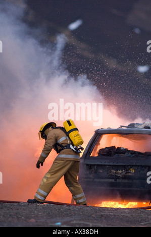 Un pompier portant un appareil respiratoire s'attaquer à un véhicule en feu Banque D'Images