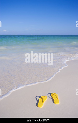 Paire de sandales flip flop jaune sur la plage au bord de l'eau dans les Caraïbes Banque D'Images