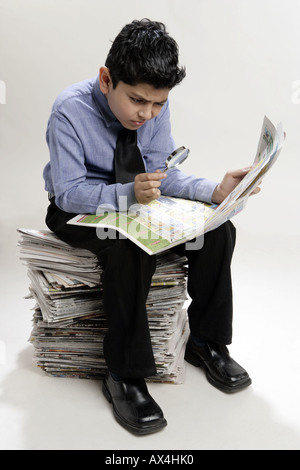 Boy holding d'une loupe et d'une recherche dans un journal Banque D'Images