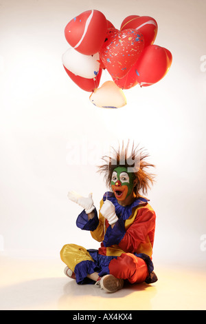 Portrait d'un joker sitting on floor and holding balloons Banque D'Images