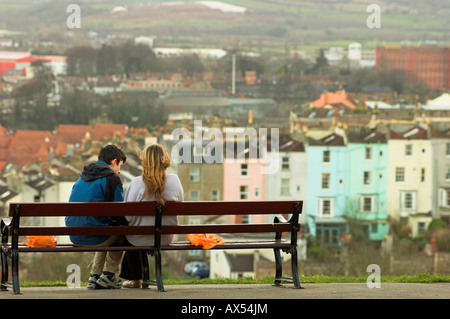 Couple assis sur un banc de parc en arrière-plan d'hiver de maisons de plus en plus floue dans la distance Banque D'Images