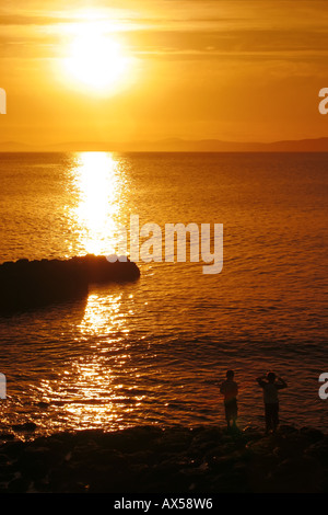 Deux jeunes garçons se tenant sur le rivage de Portrush, l'Irlande du Nord, au coucher du soleil, en regardant vers le comté de Donegal sur l'horizon Banque D'Images