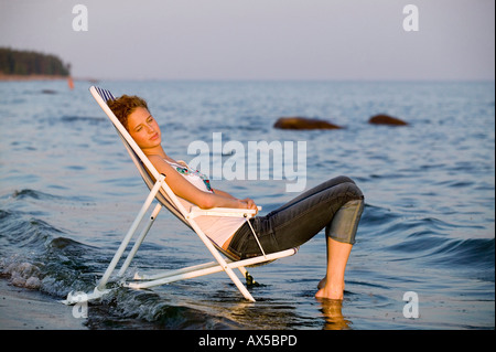 Jeune femme se reposant dans une chaise longue sur la plage, vue latérale Banque D'Images