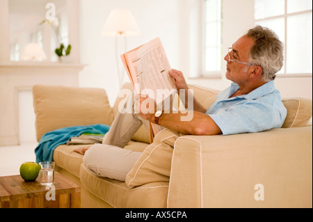 Man reading newspaper sur canapé, vue latérale Banque D'Images