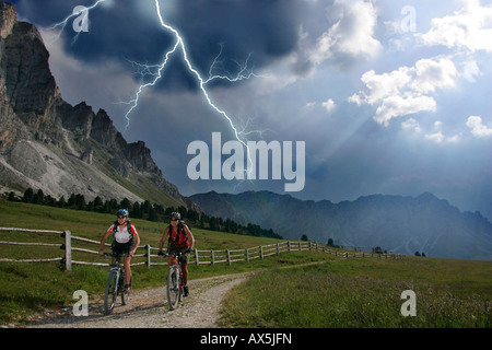 Les cyclistes de montagne femelle au cours d'un orage, la foudre en arrière-plan, Dolomites, Italie du nord, en europe Banque D'Images