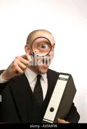 Young man carrying binder holding magnifying glass en face de son visage Banque D'Images