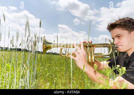 Jeune homme jouant de la trompette en champ, side view Banque D'Images