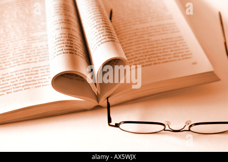 Livre ouvert, pages en forme de cœur avec lunettes de lecture et d'un signet Banque D'Images