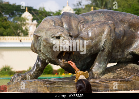 Petite fille indienne de toucher une statue en bronze d'un lion OU tigre de grincement dans les motifs de Mysore Palace Banque D'Images