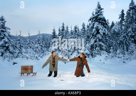 Jeune couple carrying Christmas Gift on sled in snow Banque D'Images