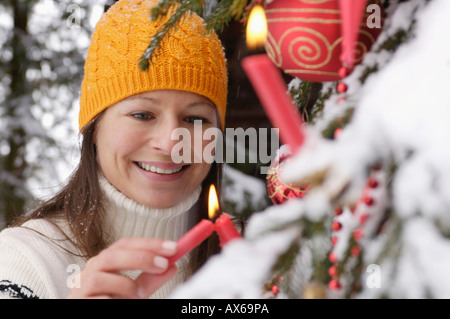 Young woman decorating Christmas Tree in snow, smiling Banque D'Images