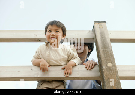 Un petit garçon se reflète de balustrade de bois comme son père regarde sur Banque D'Images