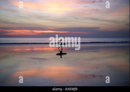 Coucher du soleil sur la plage de Kuta surfers portent leurs planches de surf de l'océan après une longue journée à cheval les vagues Banque D'Images