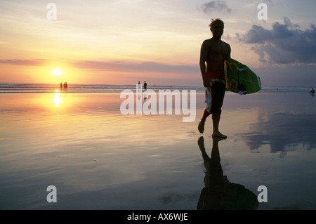 Coucher du soleil sur la plage de Kuta surfers portent leurs planches de surf de l'océan après une longue journée à cheval les vagues Banque D'Images