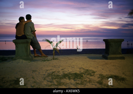 Un jeune couple se trouve près de la plage pendant le coucher du soleil à Kuta Beach Bali Indonésie Banque D'Images