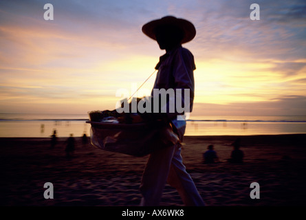 Un vendeur à vendre des babioles et des collations promenades le long de la plage de Kuta Bali, Indonésie Banque D'Images