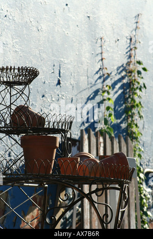 Pots de fleurs vides assis sur un piédestal à côté de grandes fleurs et clôture blanche le long d'un mur de ciment bleu. Banque D'Images